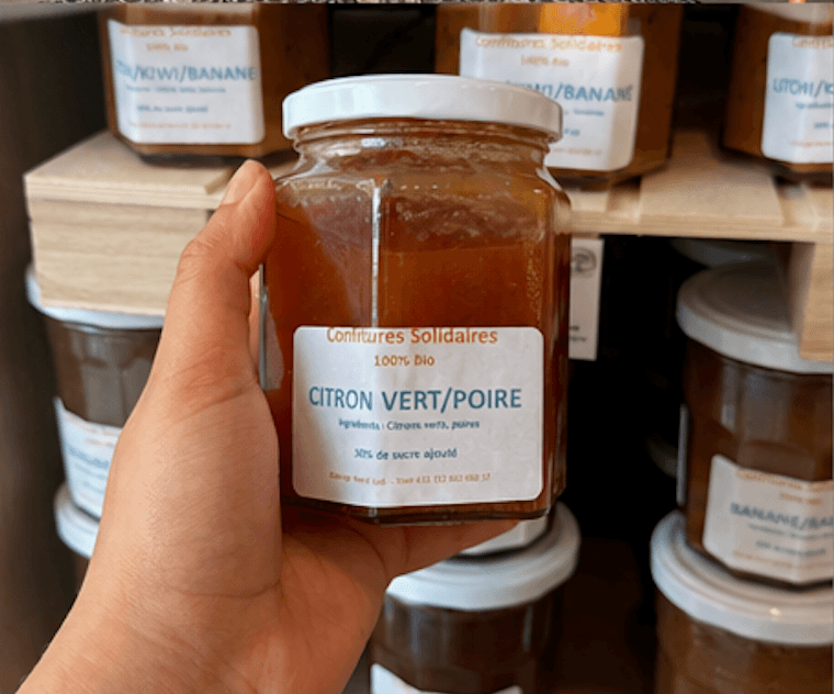 Main tenant un pot de confiture bio citron vert et poire sur une étagère.