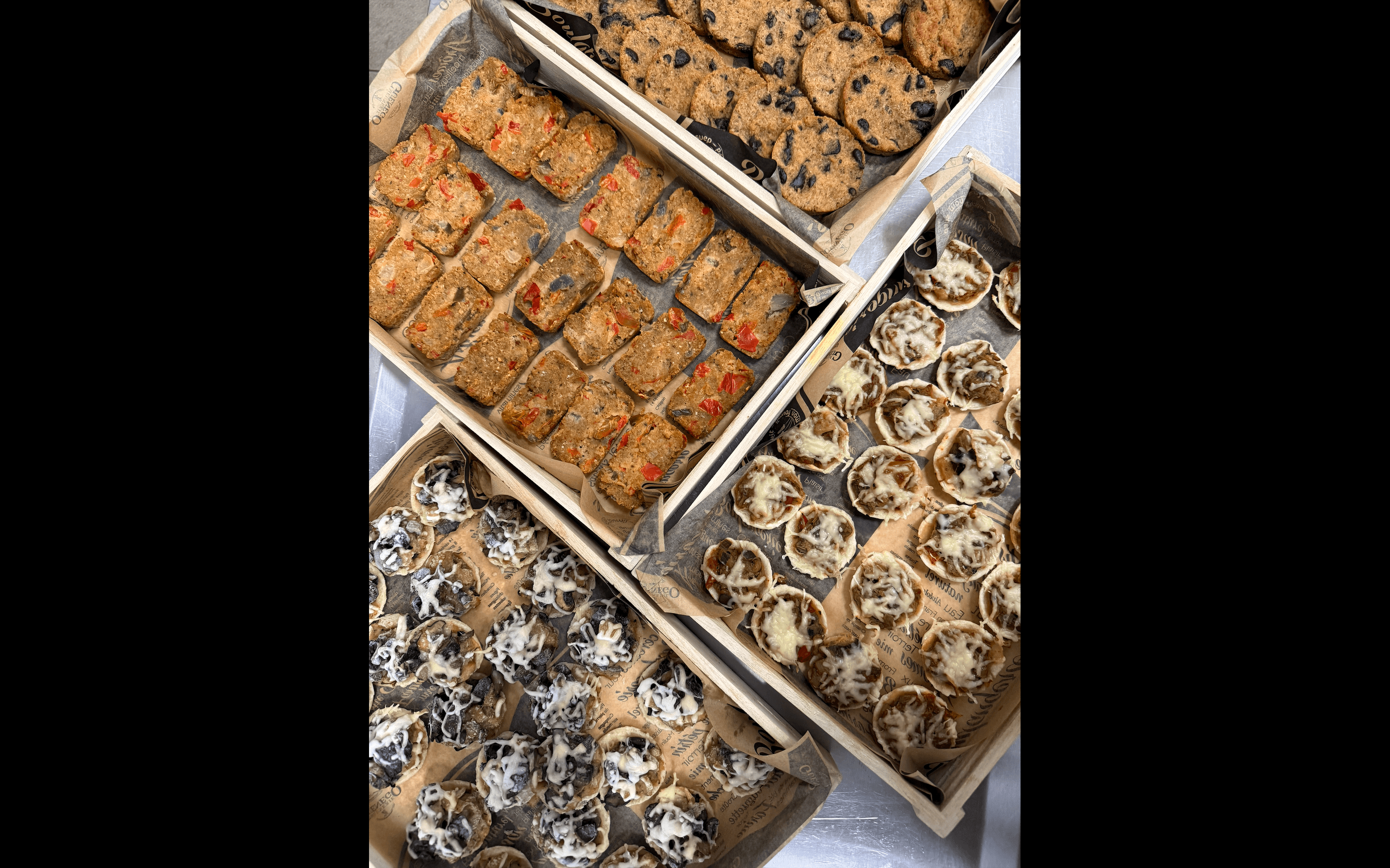 Cookies au chocolat, bouchées aux poivrons et mini-tartes salées disposés dans quatre caisses en bois.