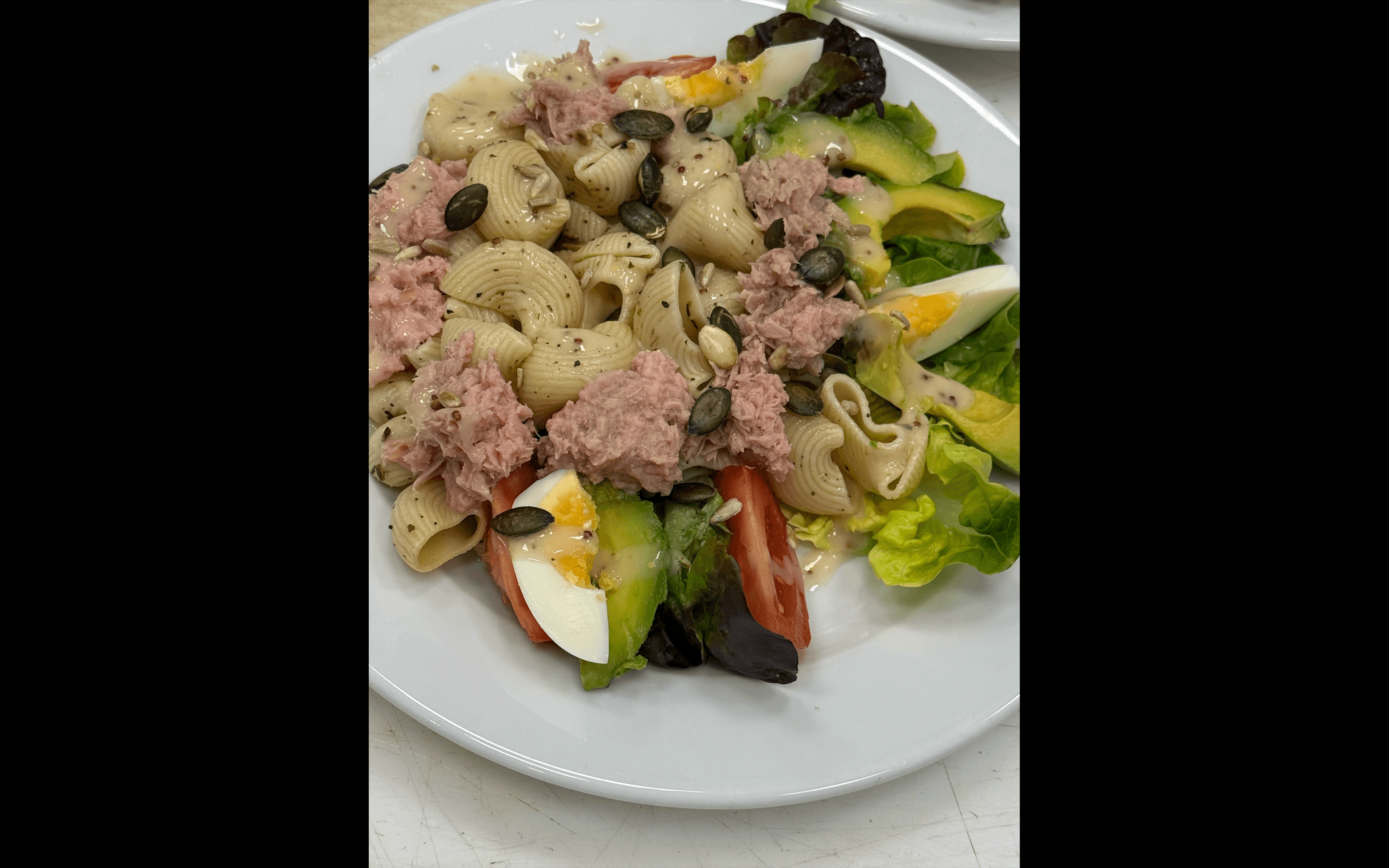 Salade de pâtes avec thon, avocat, œufs durs et tomates parsemée de graines de courge.