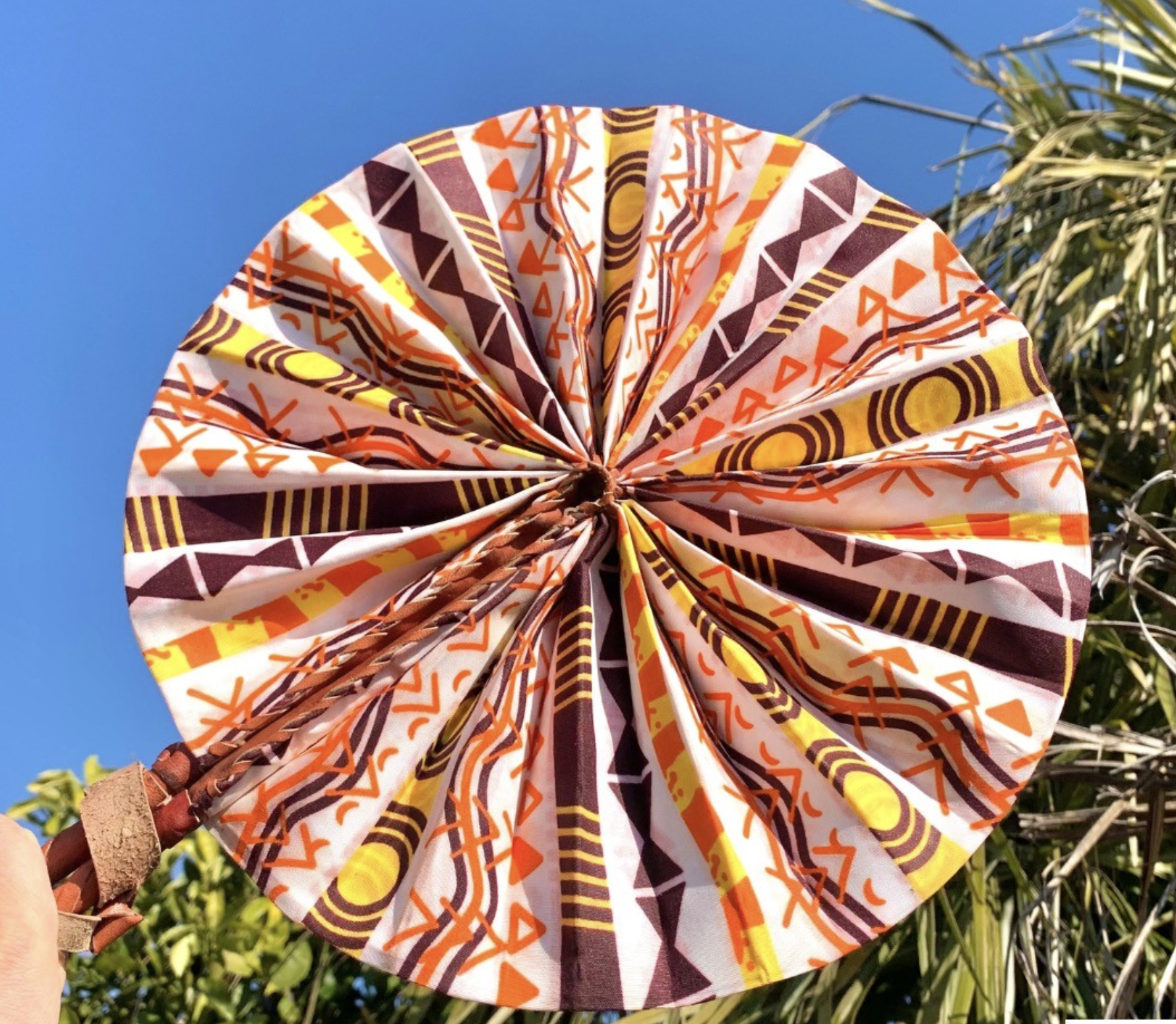 Éventail circulaire aux motifs géométriques africains orange et marron sous un ciel bleu clair.