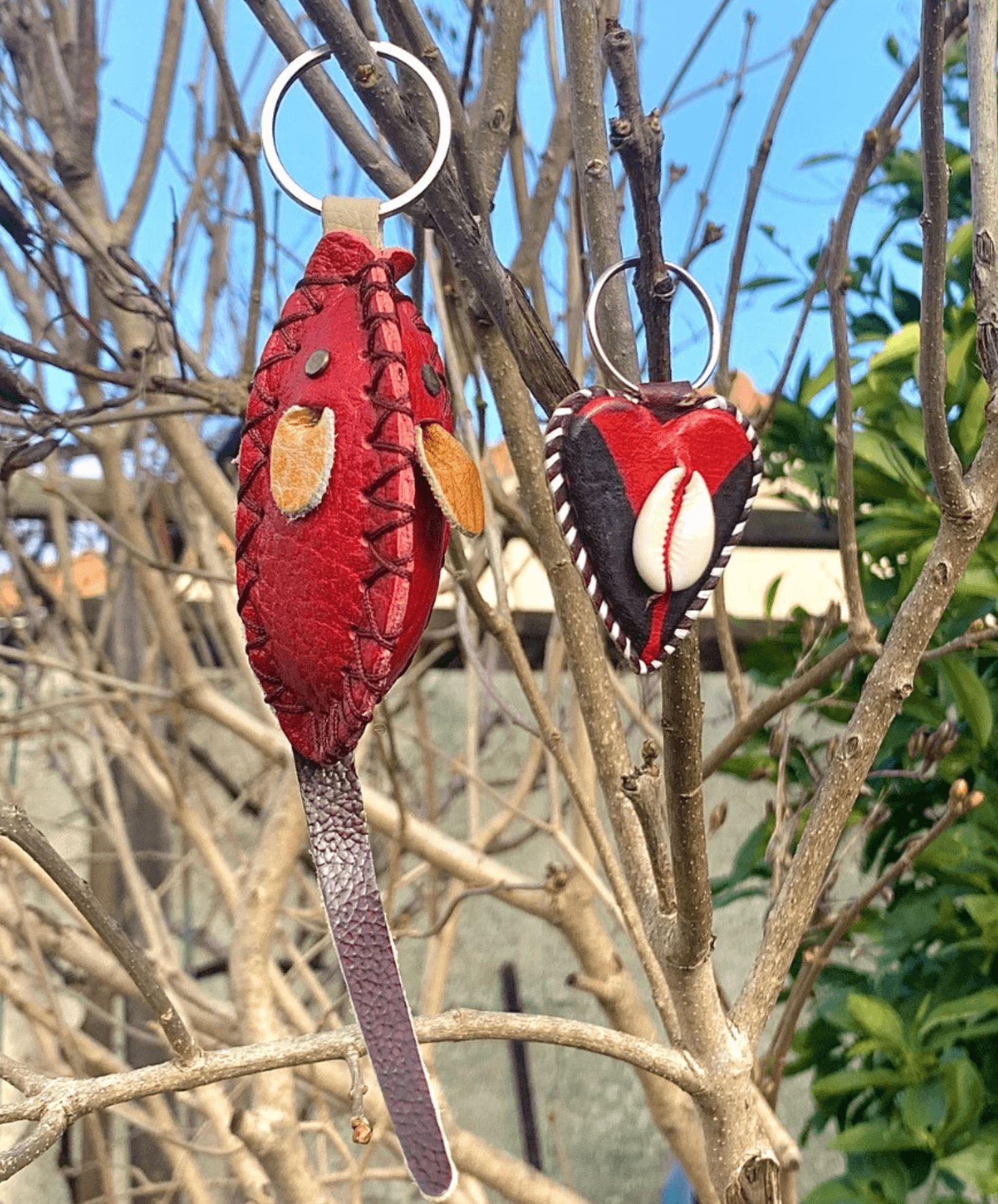 Porte-clés en cuir, souris rouge et cœur avec coquillage cauris suspendus à des branches d'arbres.