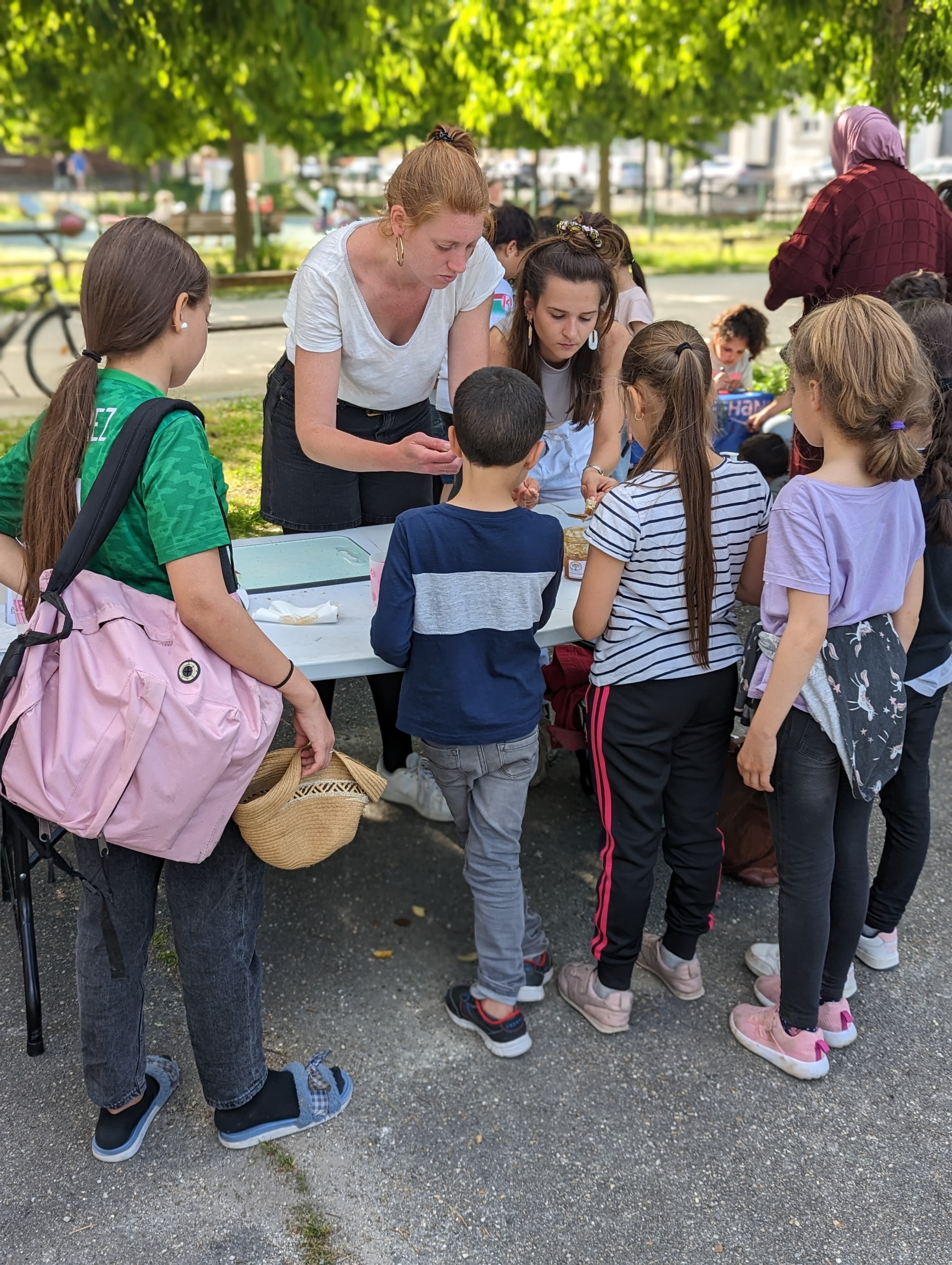 Des enfants observent deux femmes préparant de la nourriture sur une table en plein air.