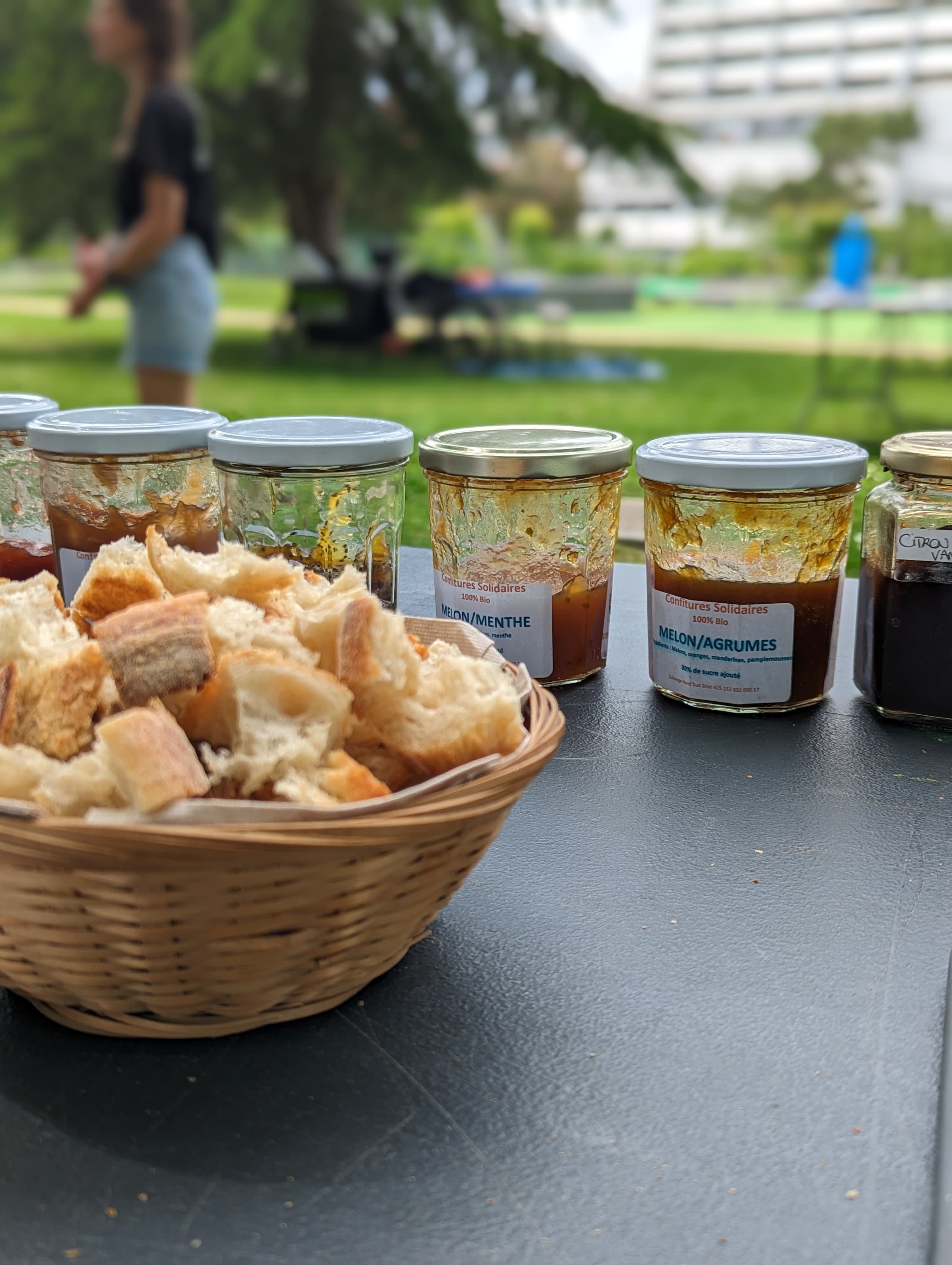 Panier de pain artisanal devant des pots de confiture bio sur une table en extérieur.